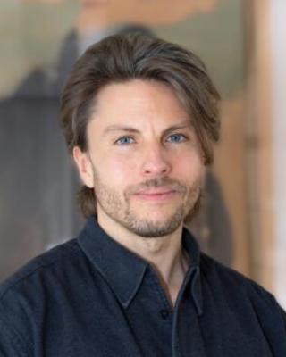 Headshot of Rouven Symank in front of a blurred background.