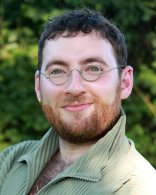 Joseph Kaplan Weinger headshot in front of shrubbery
