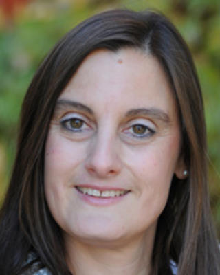 Headshot of Elke Winter taken in front of a blurred background with greenery
