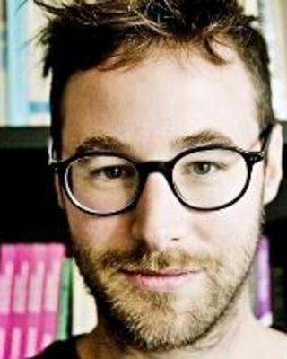 Headshot of Kobe De Keere standing by bookshelf smiling