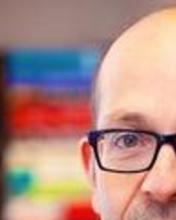 Headshot of Ron Levi standing by a bookshelf
