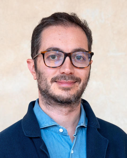 Headshot of Gianluca Busilacchi in front of a beige background