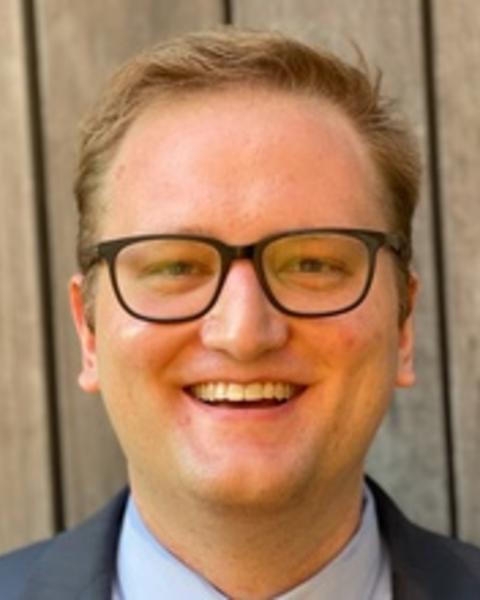 Headshot of Derek Robey in front of a wooden background