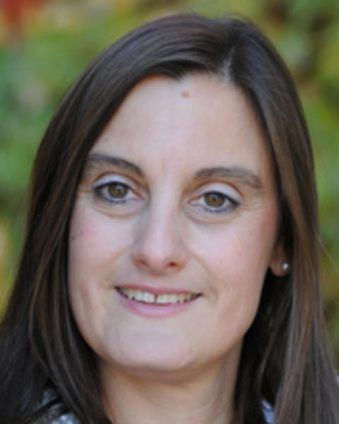 Headshot of Elke Winter taken in front of a blurred background with greenery
