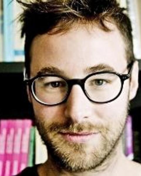 Headshot of Kobe De Keere standing by bookshelf smiling