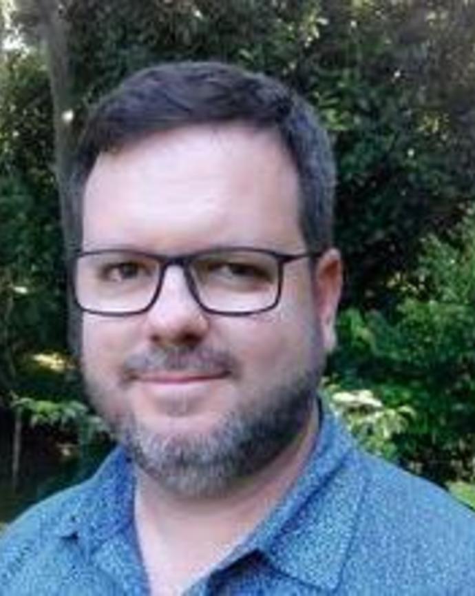 Headshot of Rogério Medeiros in front of greenery