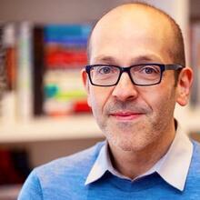 Headshot of Ron Levi standing by a bookshelf